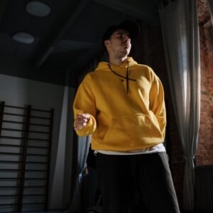 Man in yellow hoodie dancing indoors with dramatic lighting and shadows.