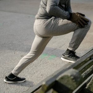 Crop anonymous male athlete wearing warm activewear stretching legs before training on asphalt road in city park in daylight